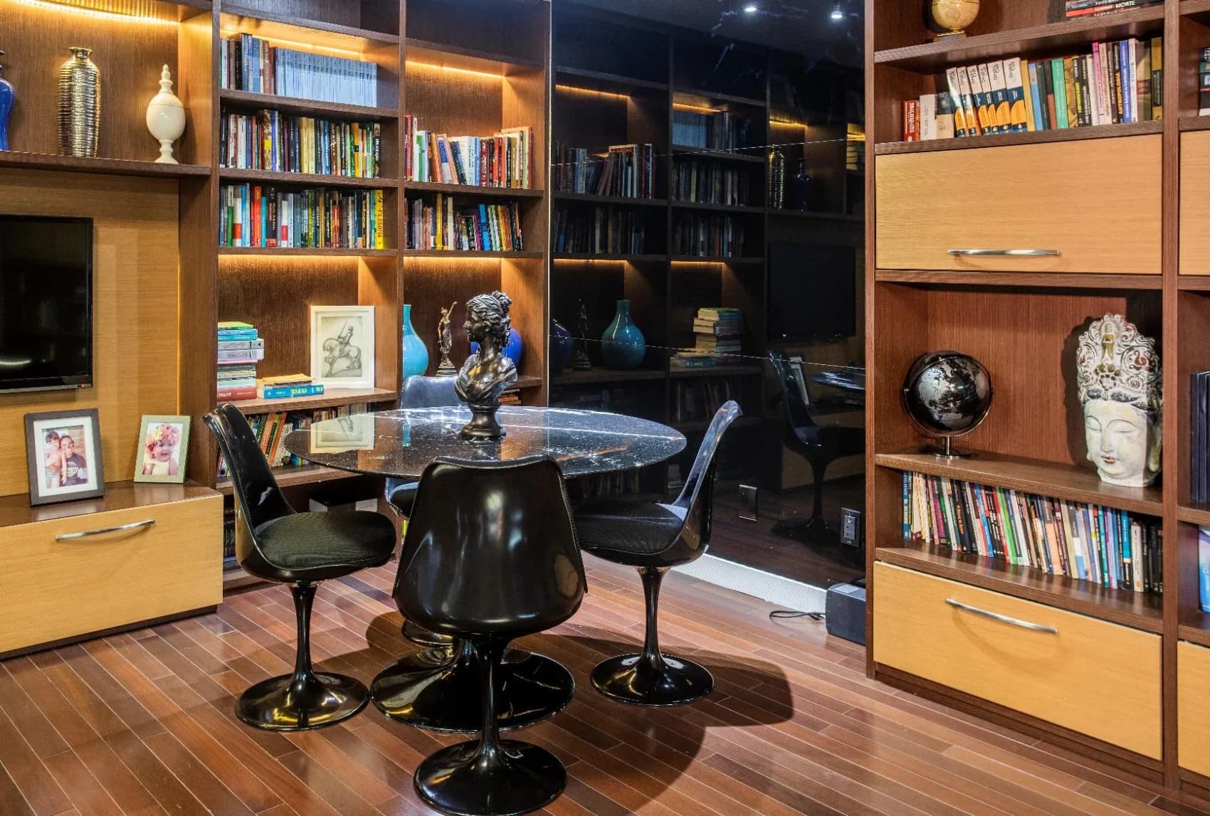 Biblioteca da banca com estantes de madeira repletas de obras, mesa de mármore e ambiente de estudo.