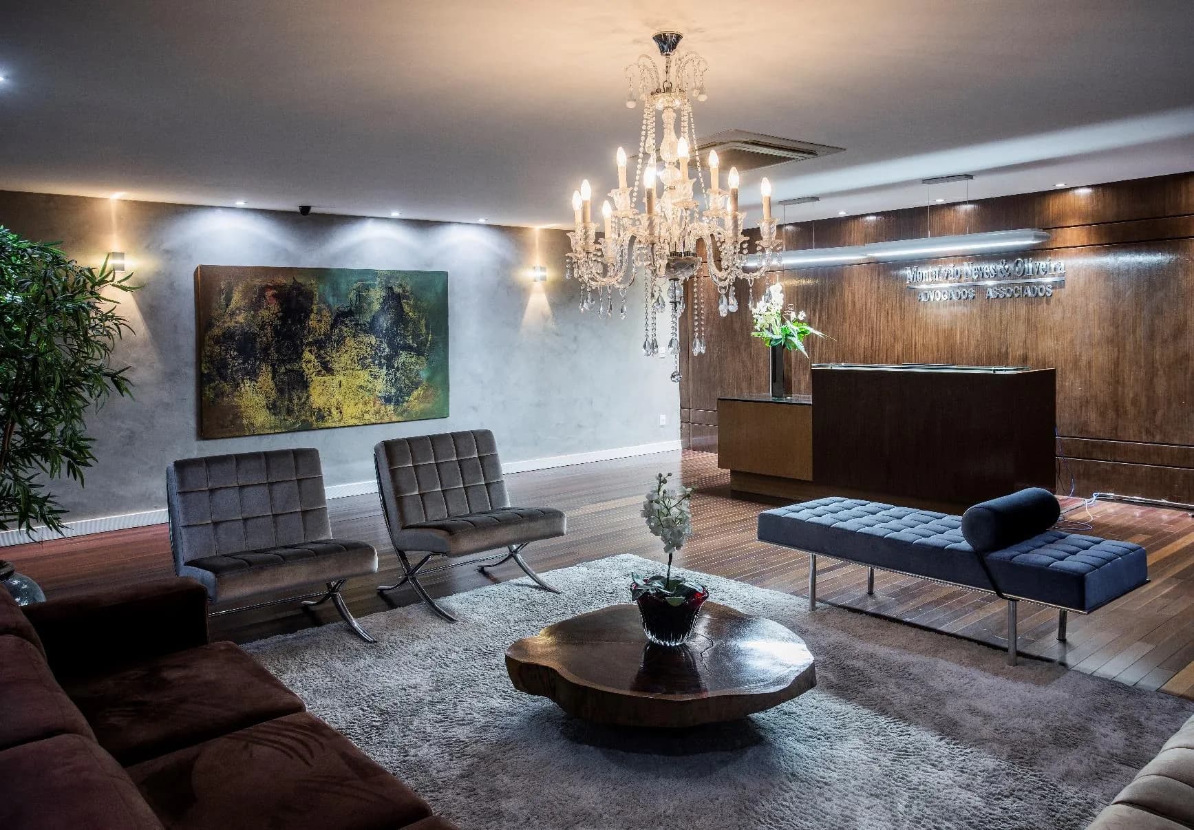 Recepção do escritório com lustre de cristal, poltronas e obra de arte na parede.